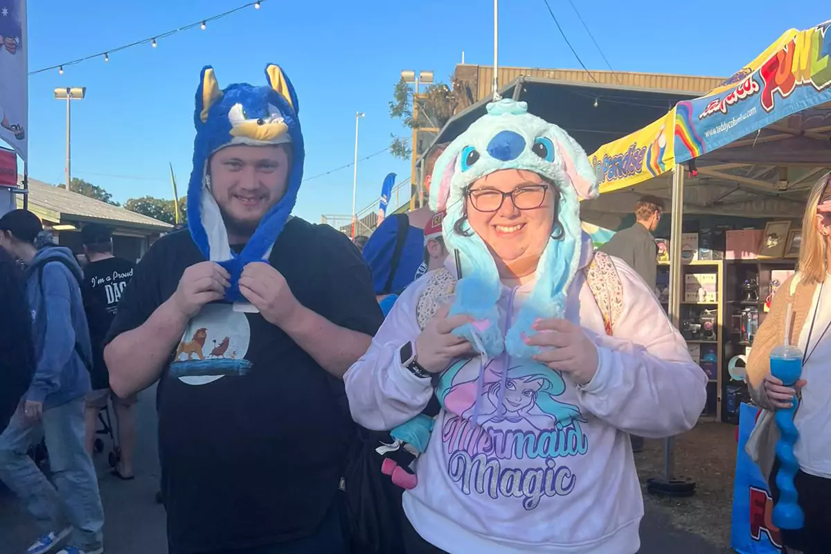 Two friends smiling while posing for a picture and holding their cartoon hats