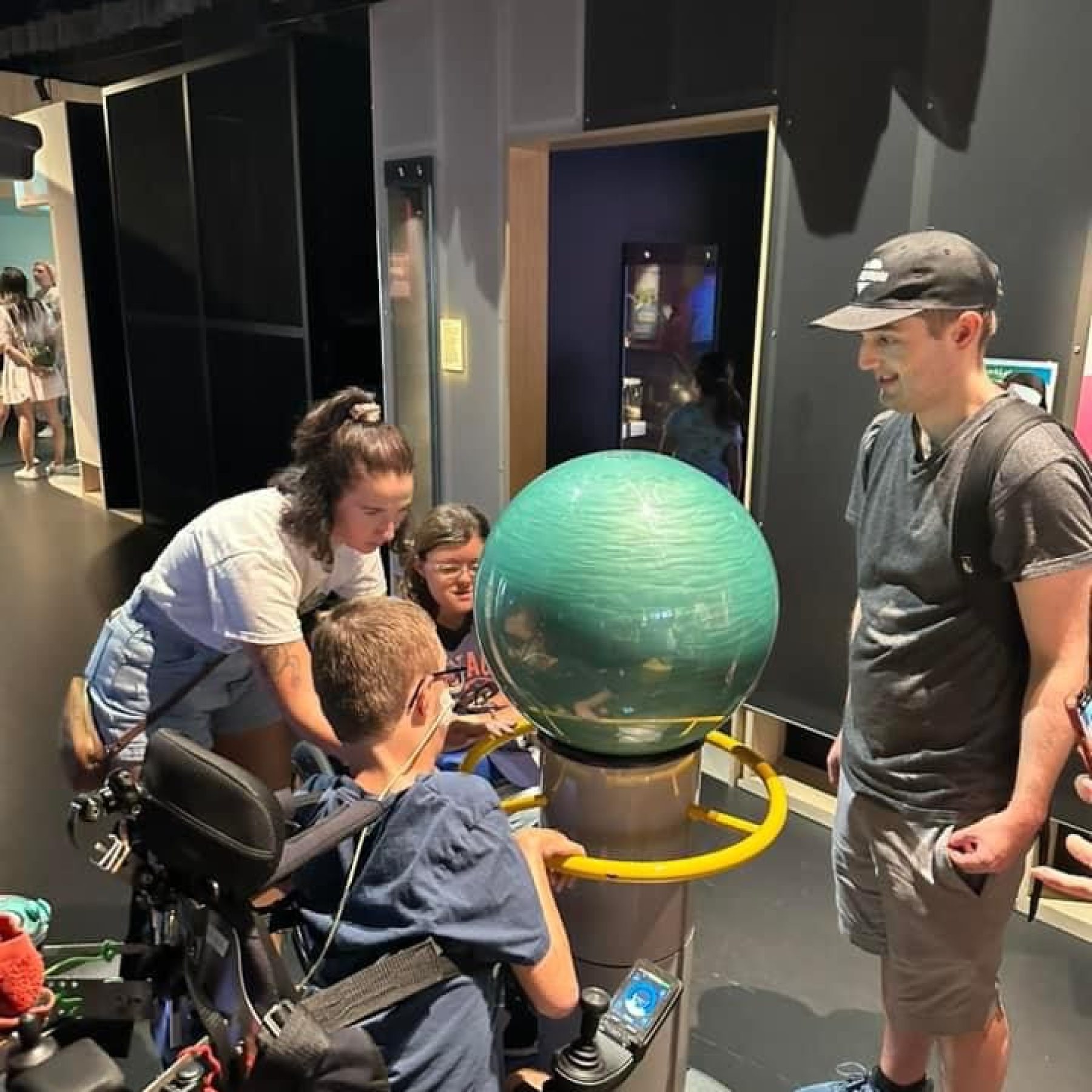 A disabled man and woman sitting in their wheelchair and their support worker looking at a green circle
