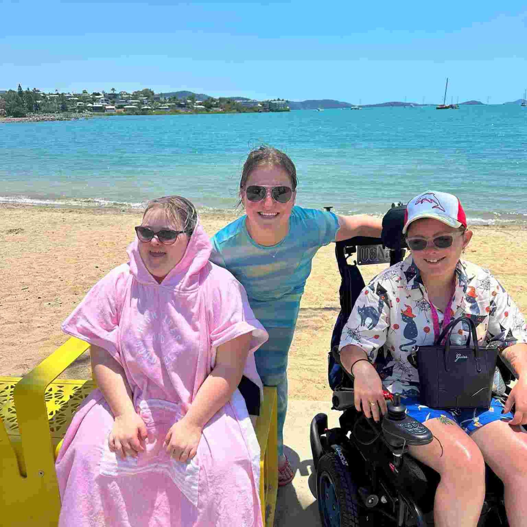Two disabled person sitting in their wheelchair and their support worker on the beach